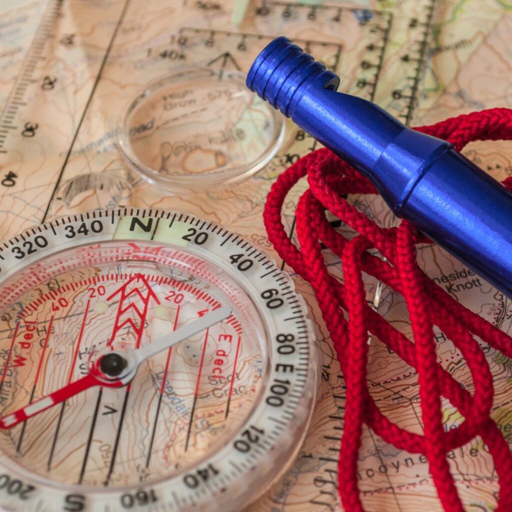 compass and whistle on top of paper map